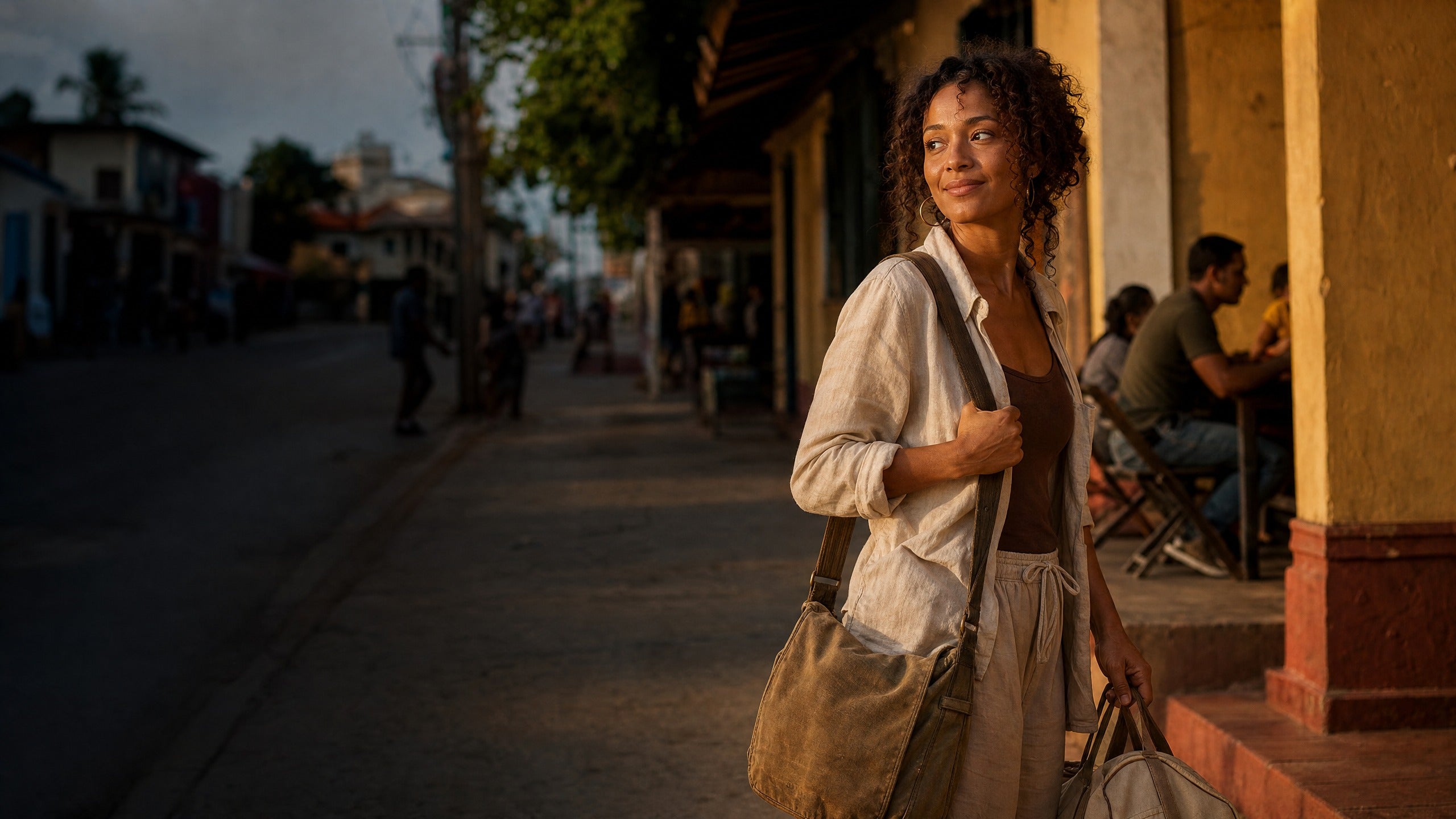 Traveller outside a Caribbean café at golden hour, carrying two bags.