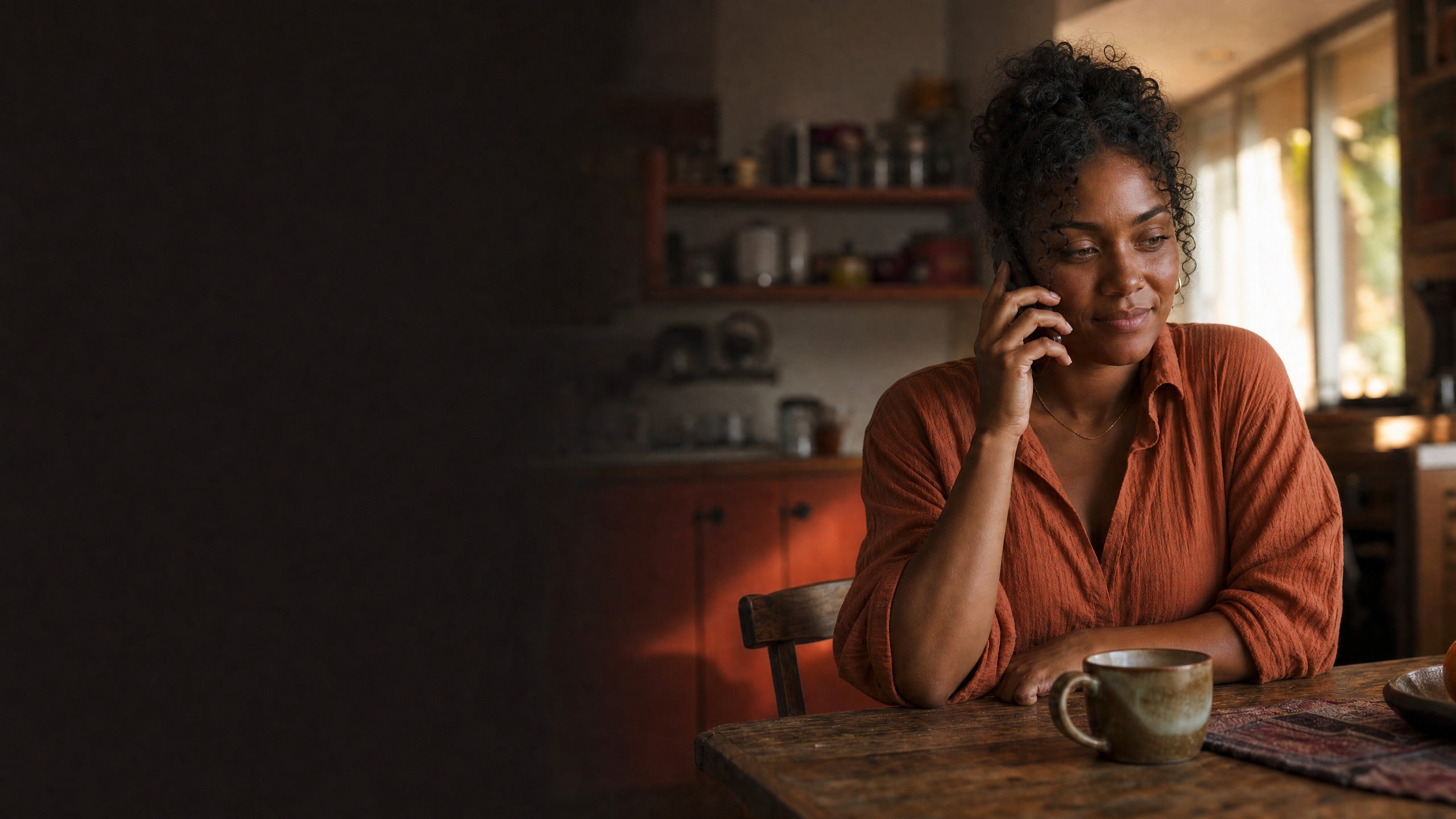 Woman in a warm kitchen listening carefully to a phone call.